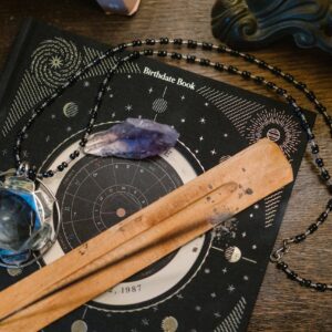 Astrology-themed flat lay featuring a birthdate book, crystals, and necklace on a wooden surface.